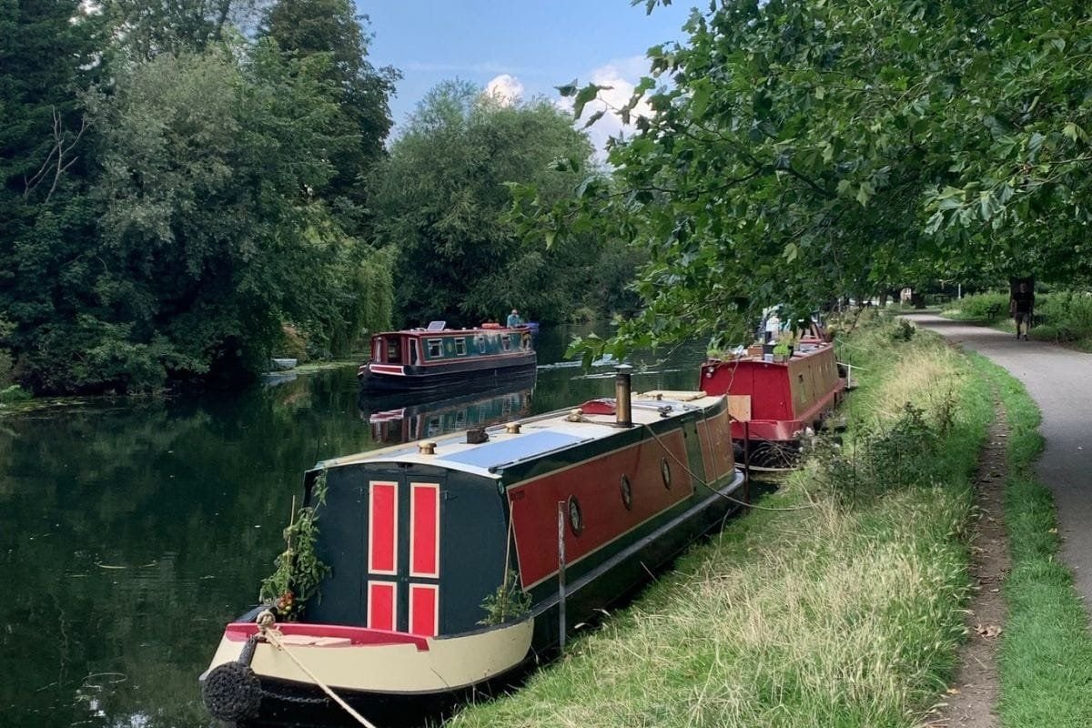 A black and red barge boat alongside the River Cam at Stourbridge Common.