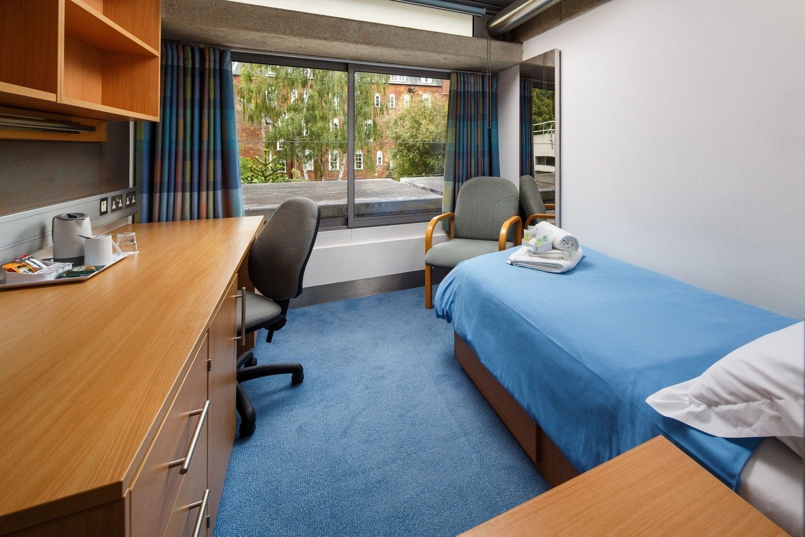 Single ensuite bedroom at Christ’s College, Cambridge, with a long desk beneath a picture window.