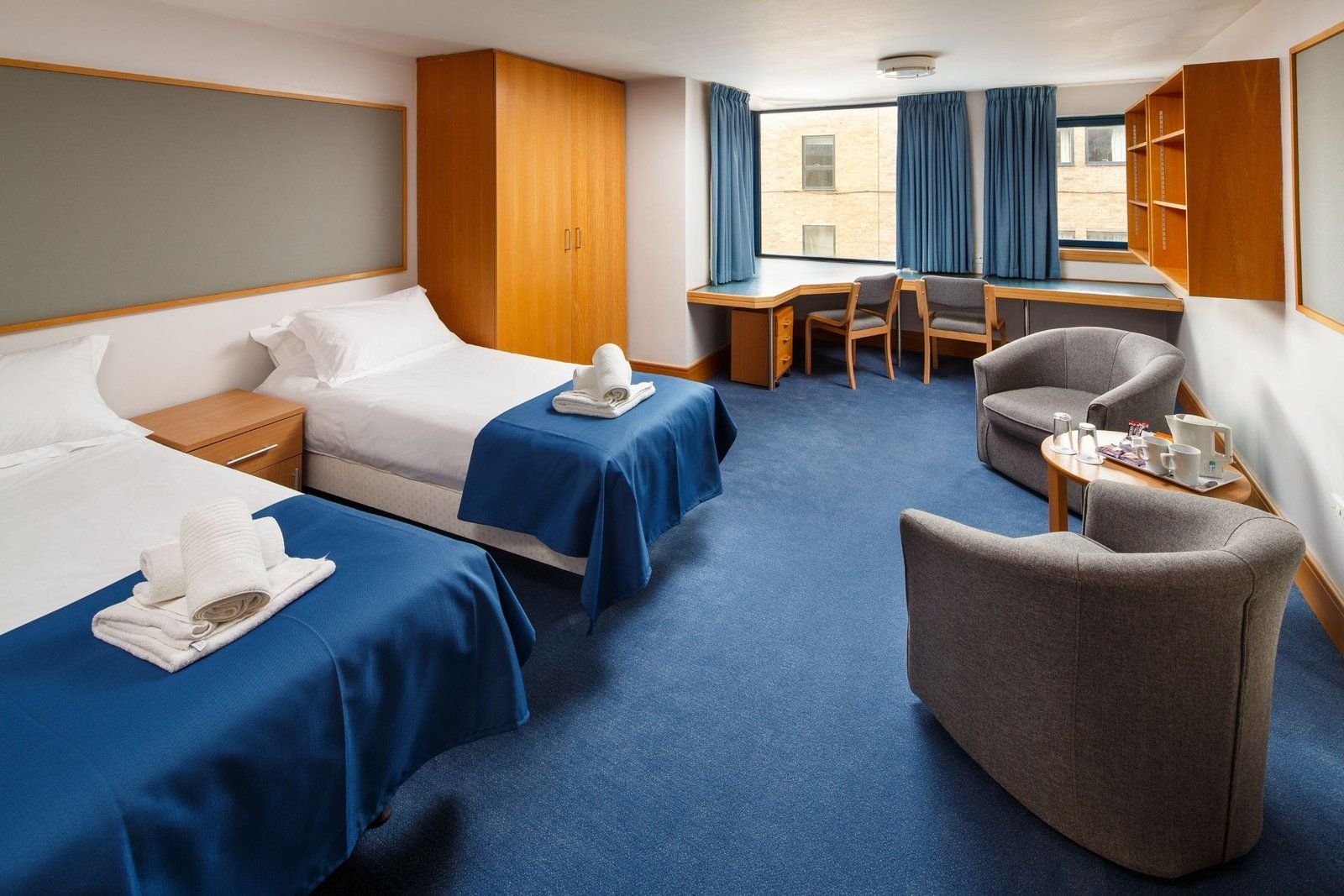 Twin ensuite bedroom at Christ’s College, Cambridge, with two single beds and blue bedspreads.
