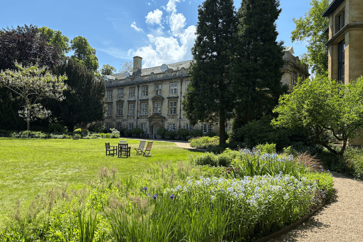 Tranquil view of the Fellows' Garden at Christ's College, Cambridge, featuring manicured lawns, vibrant flowerbeds, and mature trees surrounded by historic college buildings.