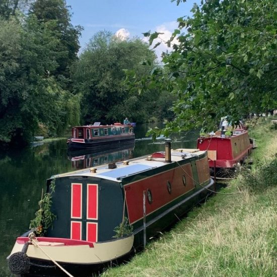A black and red barge boat alongside the River Cam at Stourbridge Common.