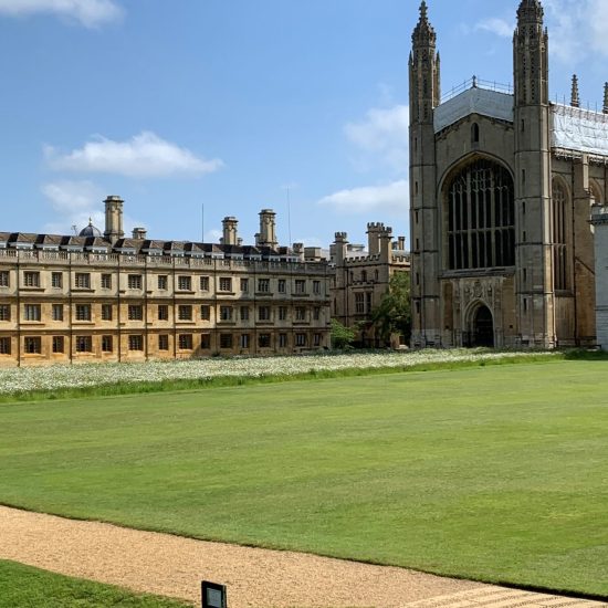 View of King’s College, Cambridge, featuring the grand Gothic architecture of King’s College Chapel with its soaring spires and large stained-glass windows, set within a manicured lawn